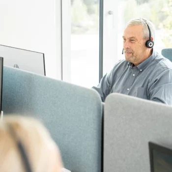 Ein Mann mit Headset sitzt vor einem PC. Hinter ihm ist ein großes Fenster.