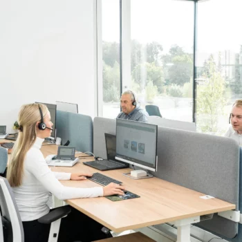 Vier Mitarbeiter von Janssen GmbH sitzen mit Headsets ausgestattet in einem Großraumbüro und arbeiten.